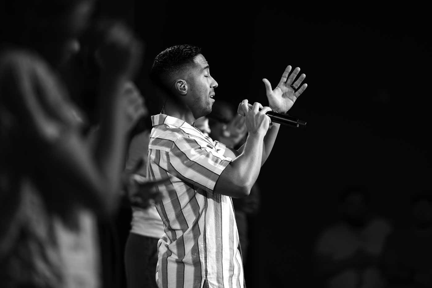 A vocalist mid-phrase, hand raised, lit from the front of house.