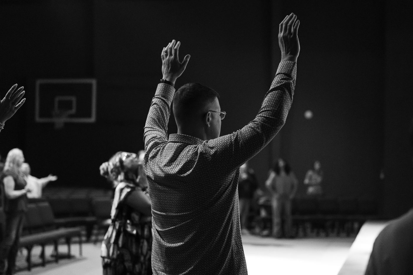 Hands raised in worship, backlit in a dark room.