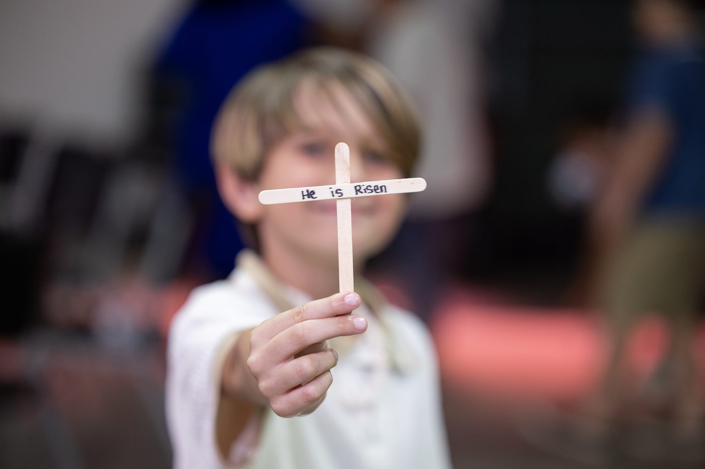 A child holding out a small wooden cross toward the camera.