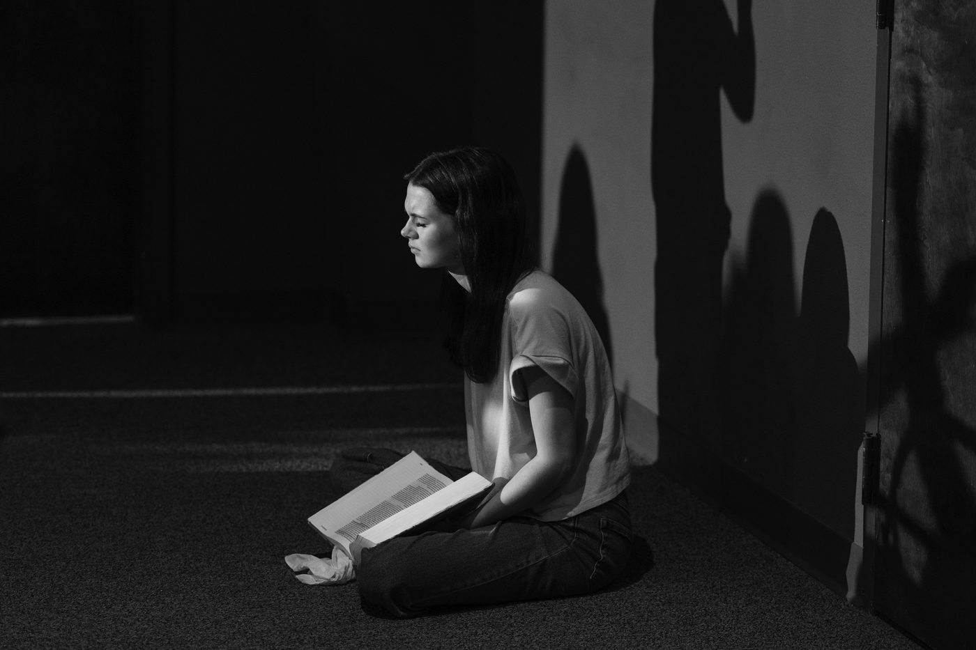 A woman kneeling with an open book in a shaft of window light.