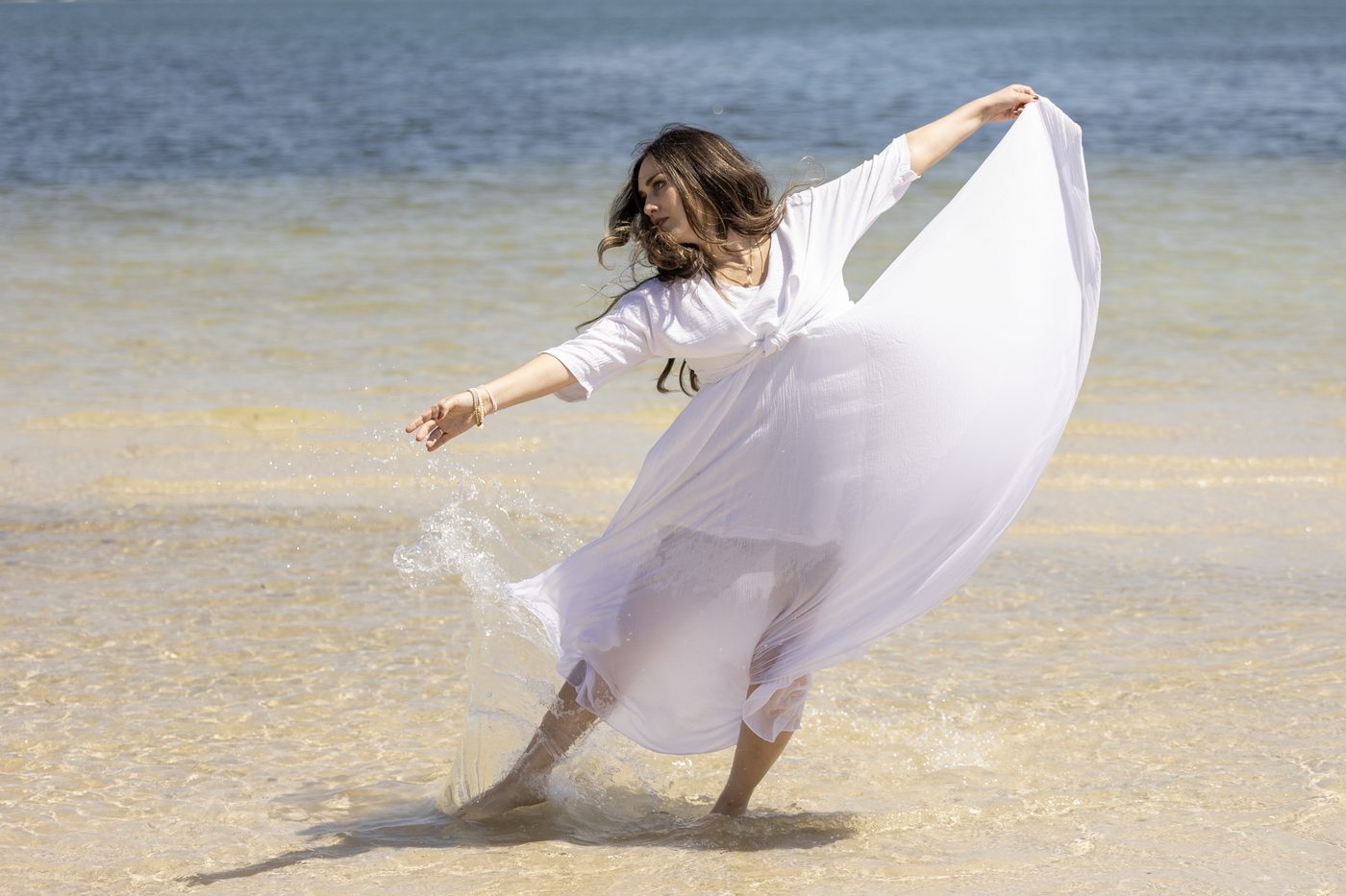 A woman in white turning in shallow water at the shoreline.